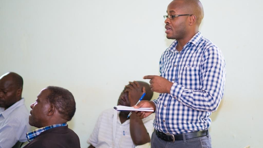 Rakai district environment officer (standing) reacts to presentations during the plenary session at the Rakai district dialogue meeting